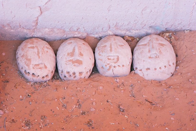 Four small sculpted clay heads at the base of a rock wall