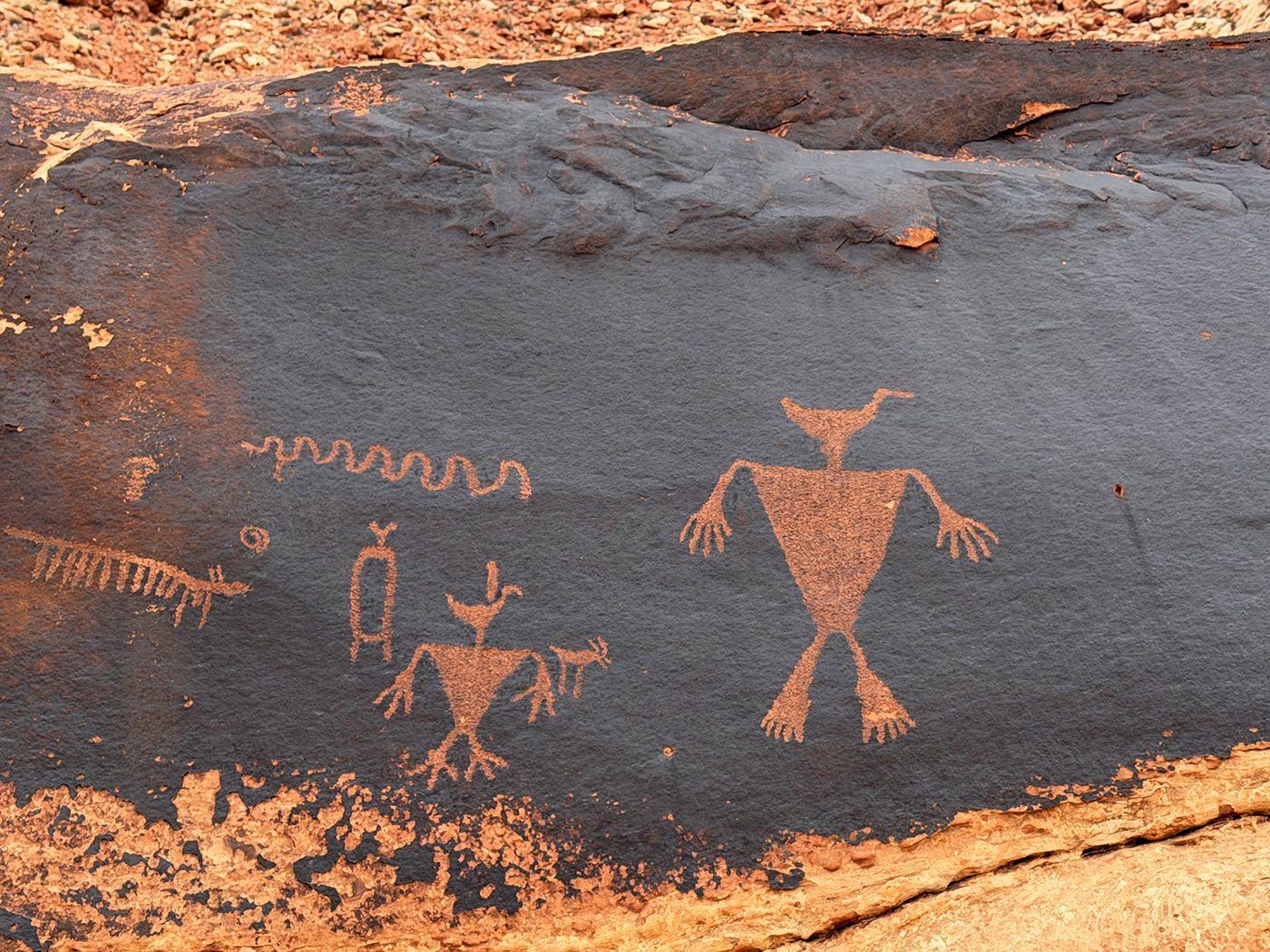 Petroglyphs on dark desert varnish: two bird-headed human figures, a wavy line and small animals