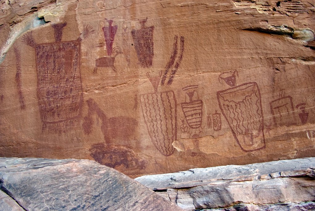Long panel of dark-red Barrier Canyon Style figures with wavy-lined and striped bodies, small animals and a bighorn sheep