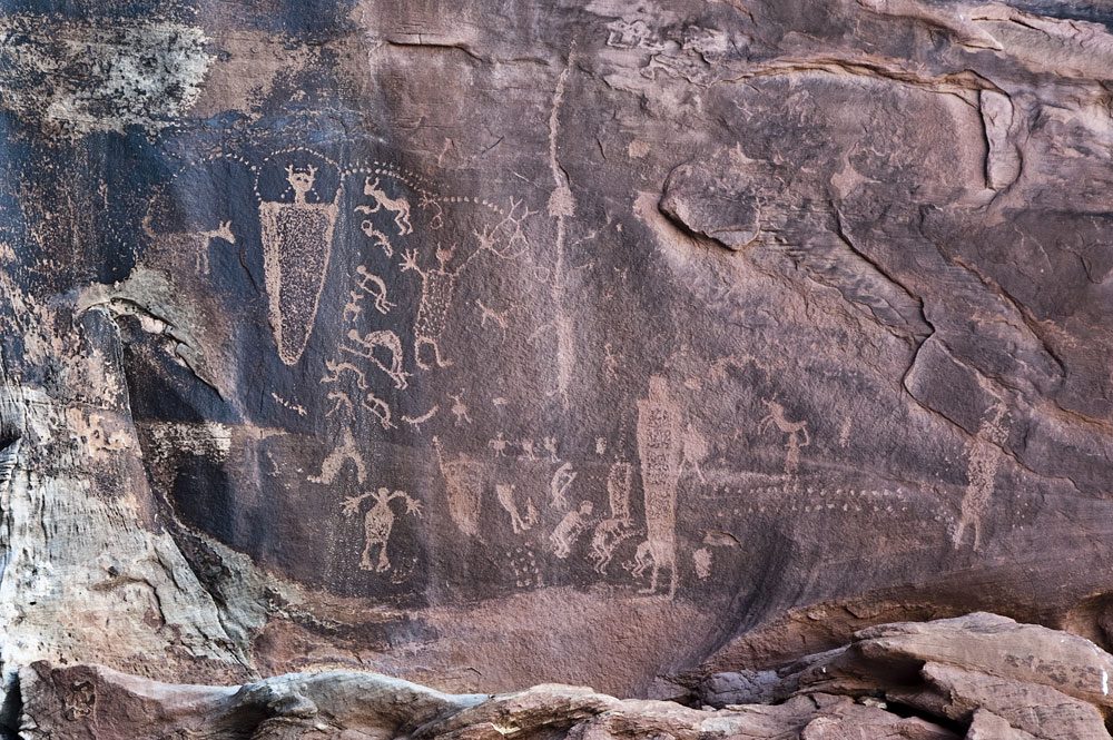 Archaic petroglyph of large figures surrounded by smaller figures, dots and a dog