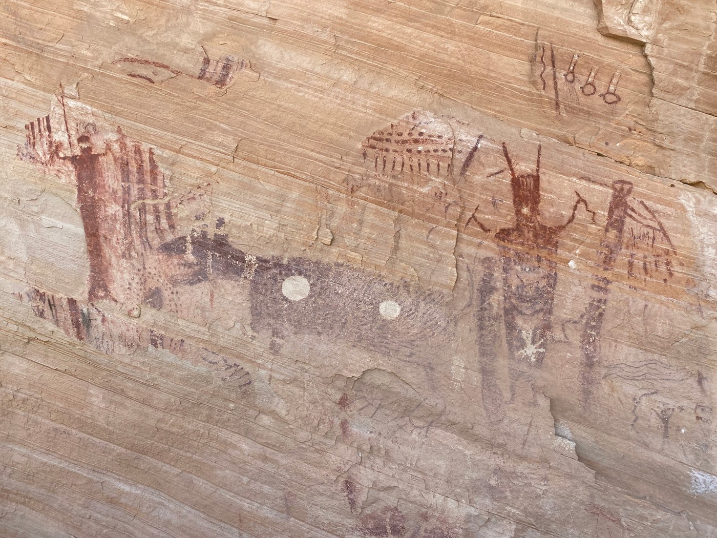 Red Barrier Canyon Style figures beside a large dark dog-like animal with two white spots, and a horned figure