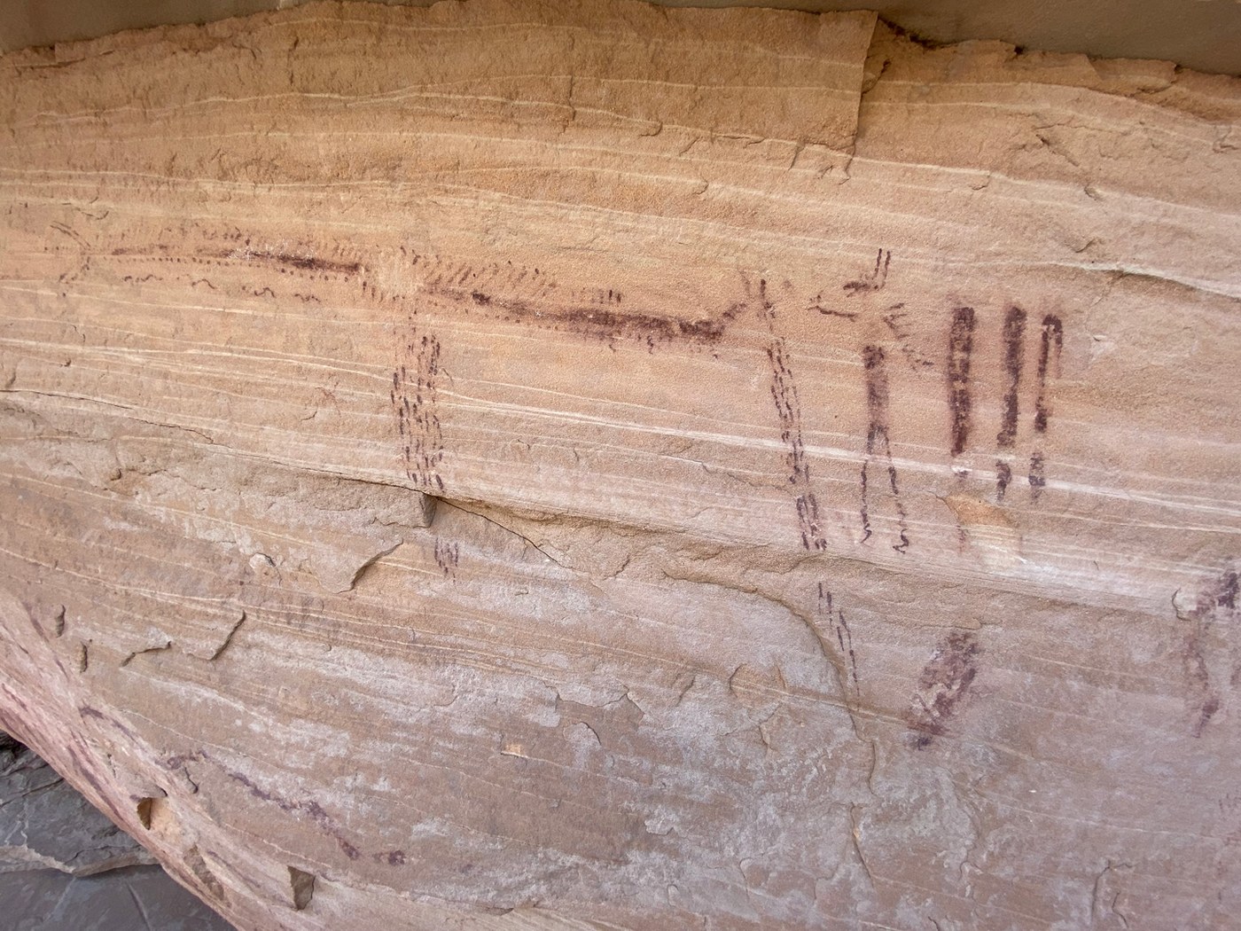 Long dotted red lines above thin vertical figures on a streaked sandstone wall