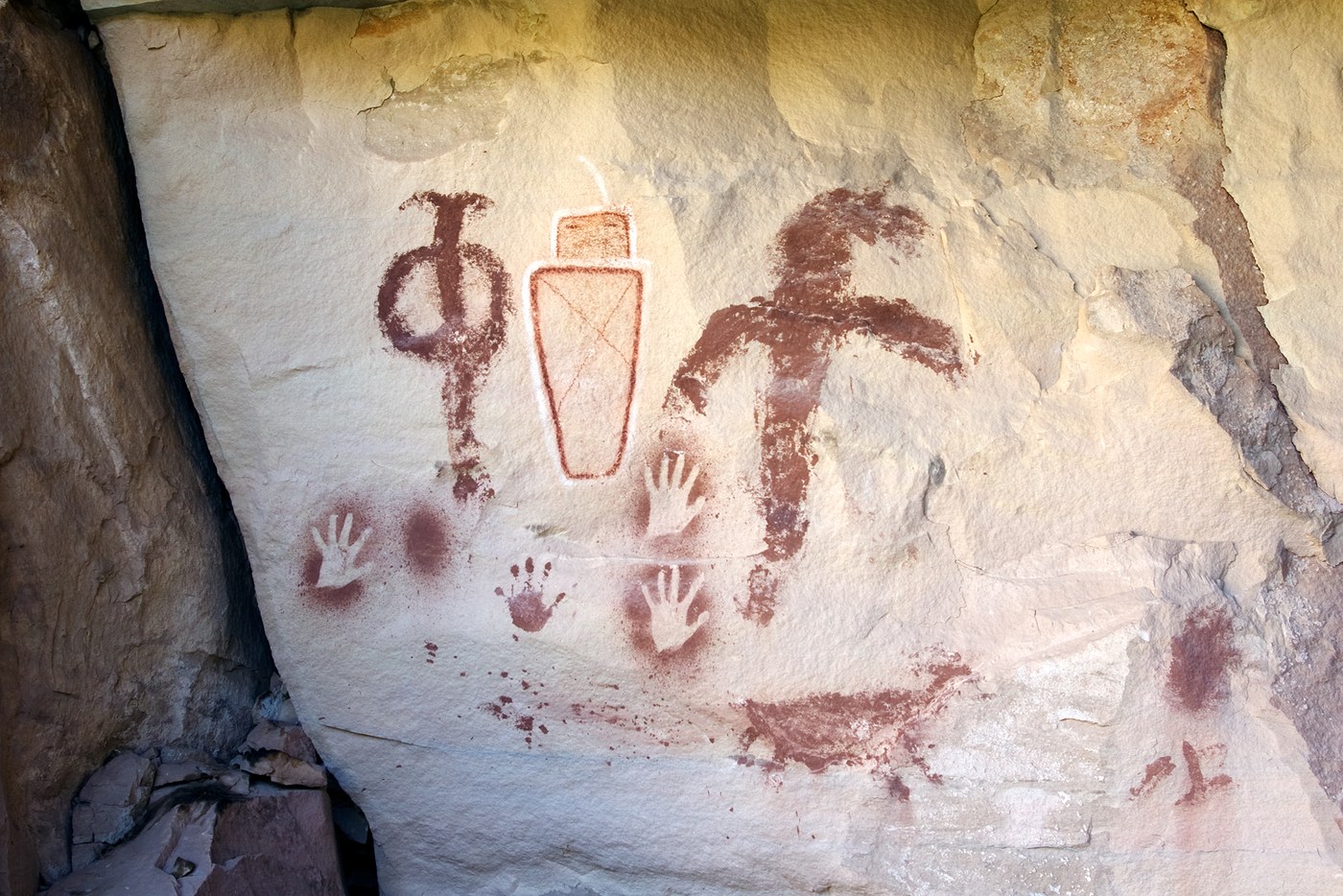A single painted face figure outlined in white, beside red pictographs and handprints