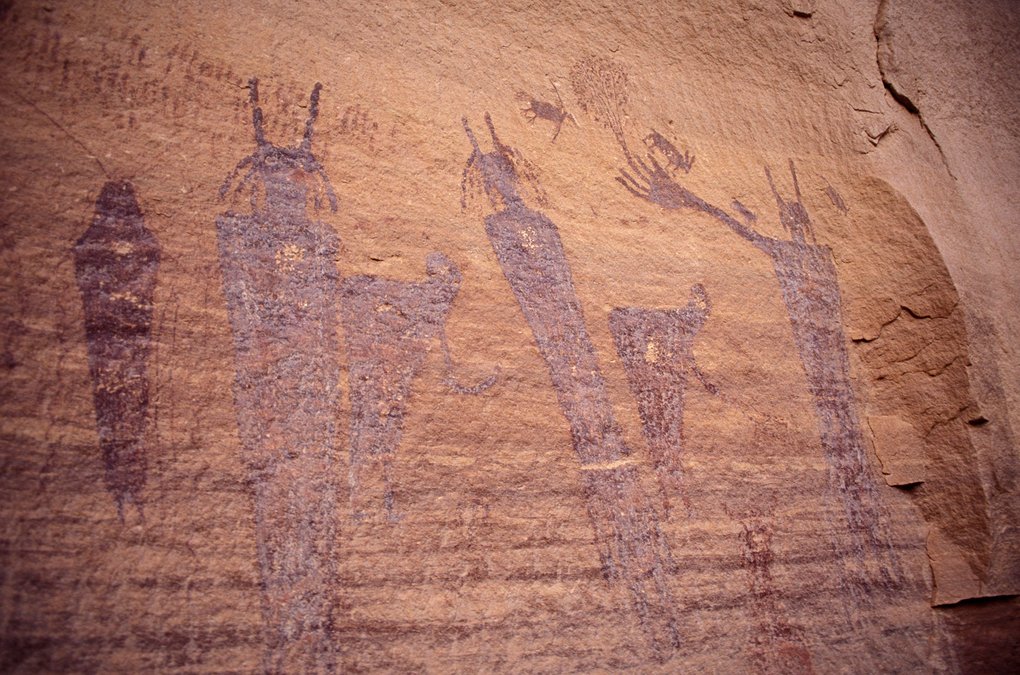 Tall Barrier Canyon Style figures with horned heads, a raised arm reaching toward a plant, and small birds