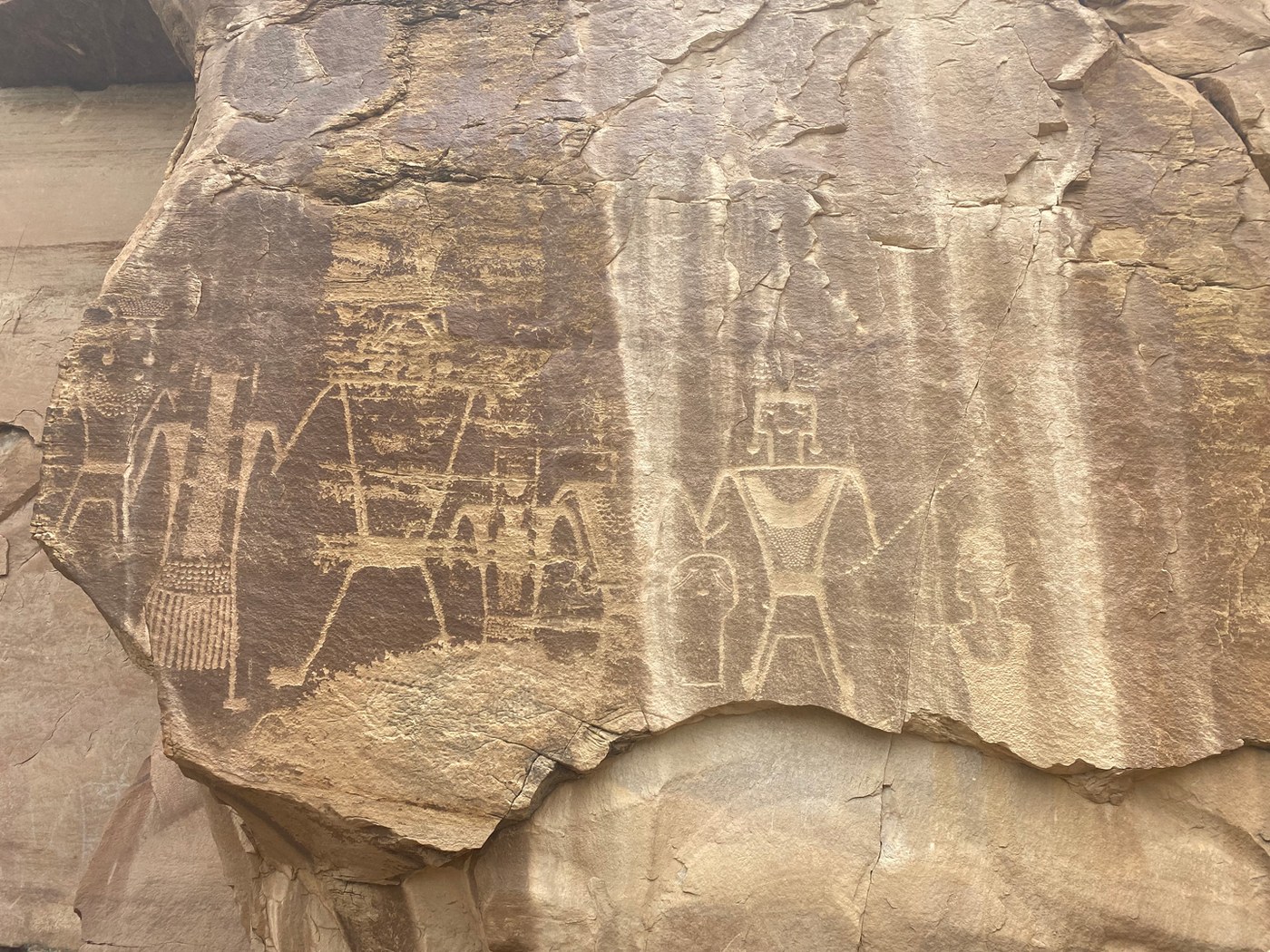 Panel of Fremont figures with headdresses and fringed objects on a streaked cliff face