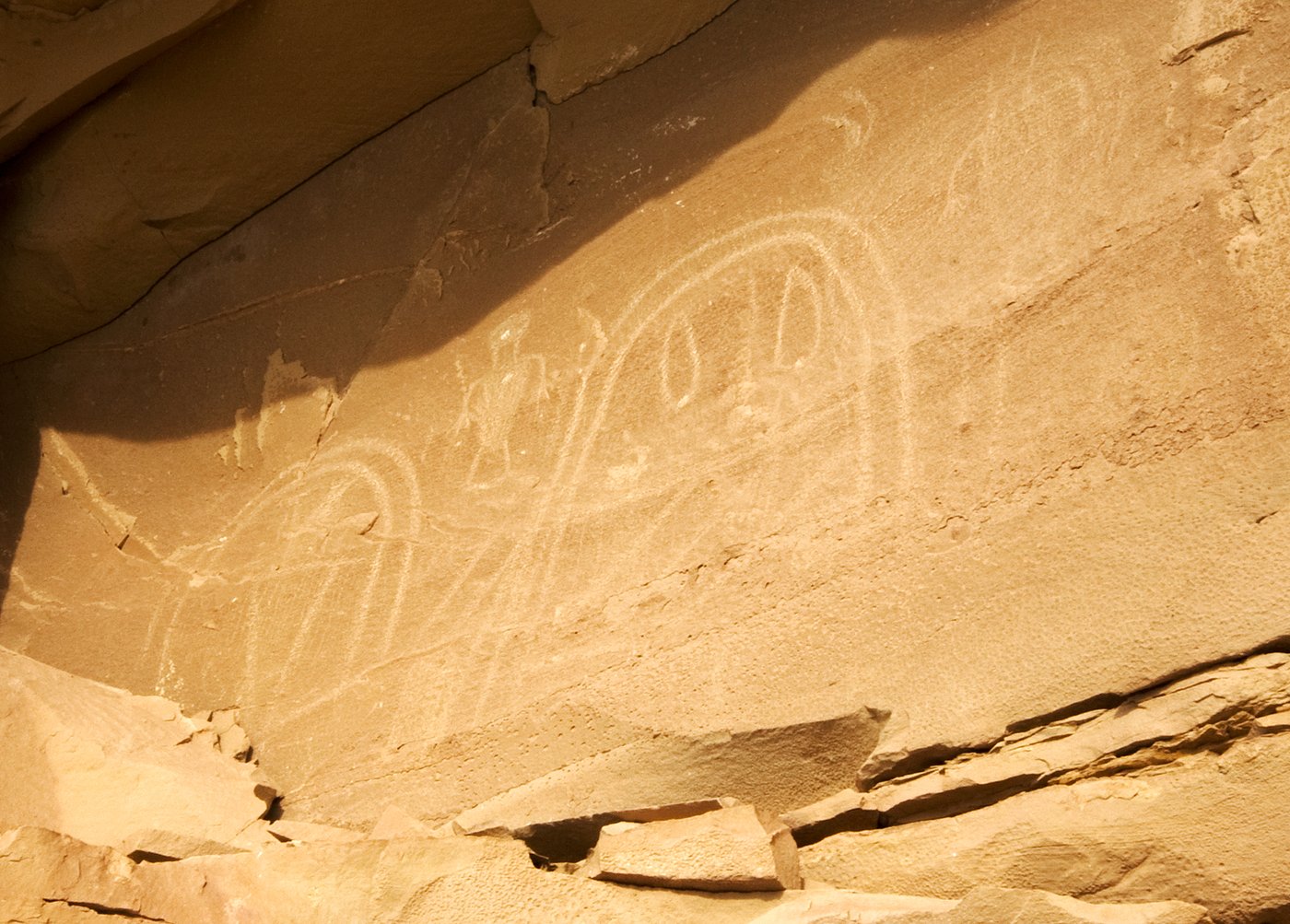 Faint pecked arch-shaped and shield-like figures on a sunlit sandstone wall